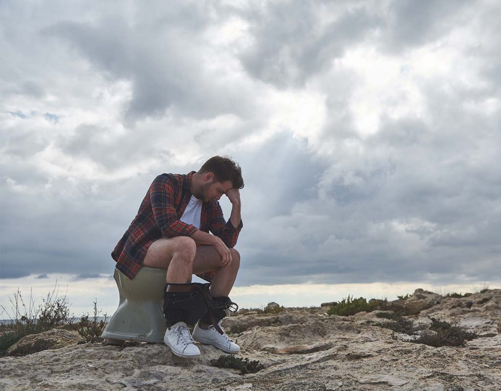 A man sits on a toilet in the outdoor wilderness. 