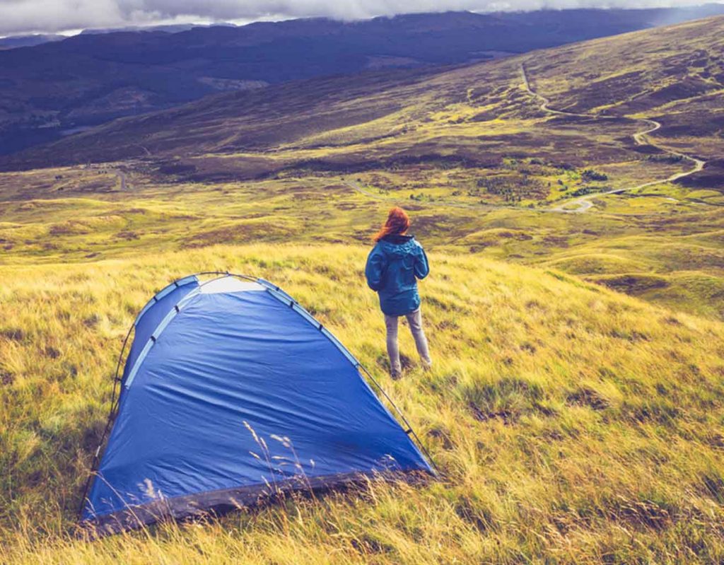 a woman stands next to her tent in the wilderness of the Scottish Highlands